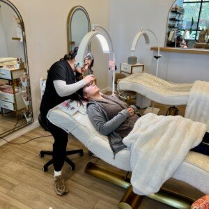 Esthetician carefully applying eyelash extensions to a reclining client on the treatment bed at LashLuv Beauty Bar in Bothell WA β serving Kenmore, Mill Creek, and Woodinville