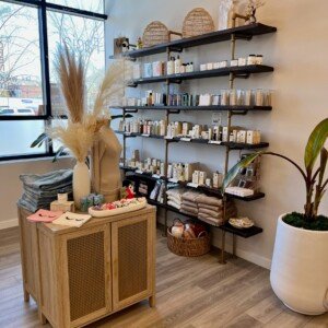 Retail wall showcasing lash, brow, waxing, and facial products with LashLuv Beauty Bar branded apparel on table – located in Bothell WA, serving Kenmore, Mill Creek, and Woodinville clients